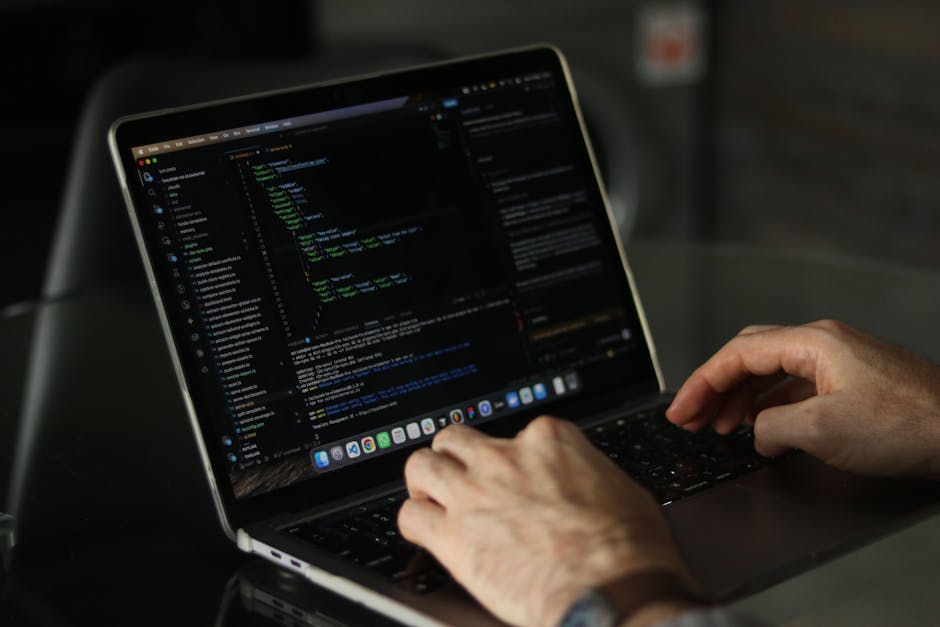 A person seated at a desk during a home relocation process, working on a silver laptop with an open code or script displayed on the screen, featuring colorful lines of text. The individual is holding